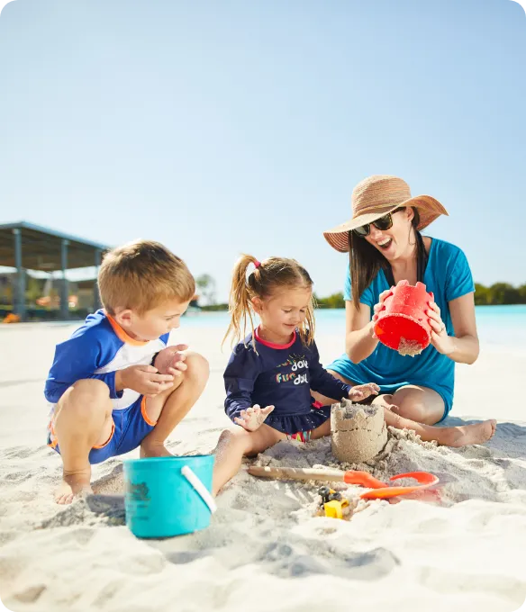 A mother and two young children build a sandcastle together on the white sand beach at Mosaic, a master-planned community in North Texas.