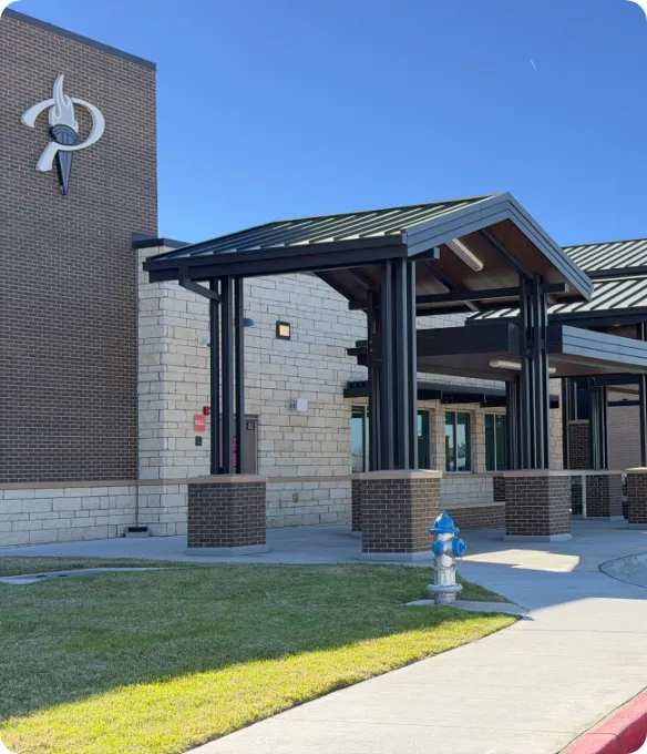 Exterior of a Prosper ISD school serving Mosaic families in Celina, Texas, with a covered entrance and brick-and-stone facade under a clear blue sky.