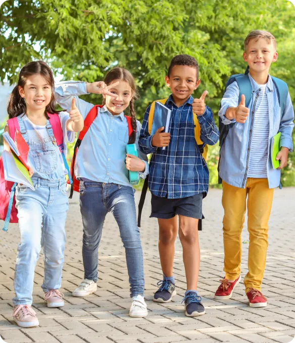 Four smiling elementary students with backpacks give a thumbs-up on their way to school, part of everyday family life at Mosaic in Celina, Texas.