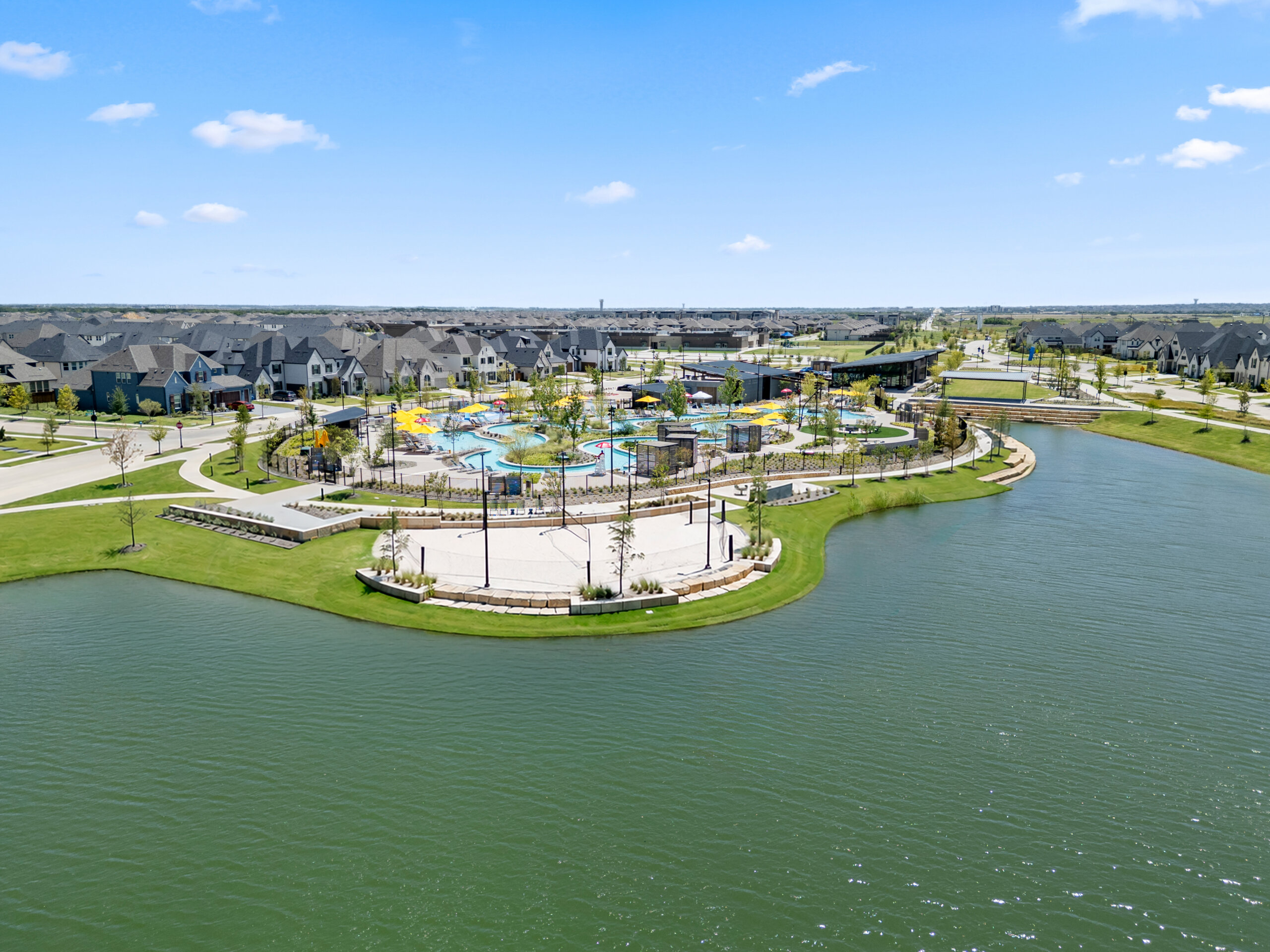 Aerial view of Mosaic in Celina, Texas, a master-planned community where lakeside sand volleyball courts, the lazy river, and the Welcome Center sit at the heart of a neighborhood of new homes.